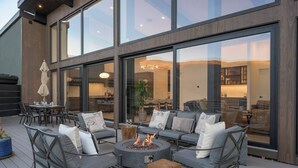 An outdoor patio with a fire pit, seating, and a view of the interior through large glass windows. - Whiskey Hill Luxury Retreat | Hot tub + Mountain Views (Vail)