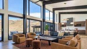 A spacious living room with a large sofa, armchairs, and ottomans, a dining area, and a kitchen with modern appliances. - Whiskey Hill Luxury Retreat | Hot tub + Mountain Views (Vail)