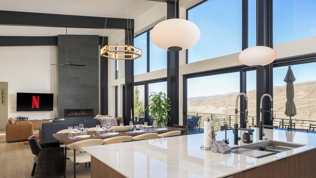 A modern kitchen with a large island, a dining area with a sofa, and a TV displaying the Netflix logo. - Whiskey Hill Luxury Retreat | Hot tub + Mountain Views (Vail)