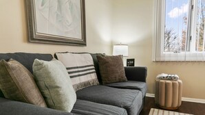 A living room with a grey sofa, multiple cushions, a framed artwork on the wall, a lamp, and a window with blinds. - Sailor`s Escape with 3 bedrooms Near Naval Base! (Waukegan)