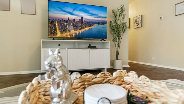 A living room with a flat-screen TV mounted on the wall, a white cabinet below it, and a decorative plant to the right. - Sailor`s Escape with 3 bedrooms Near Naval Base! (Waukegan)