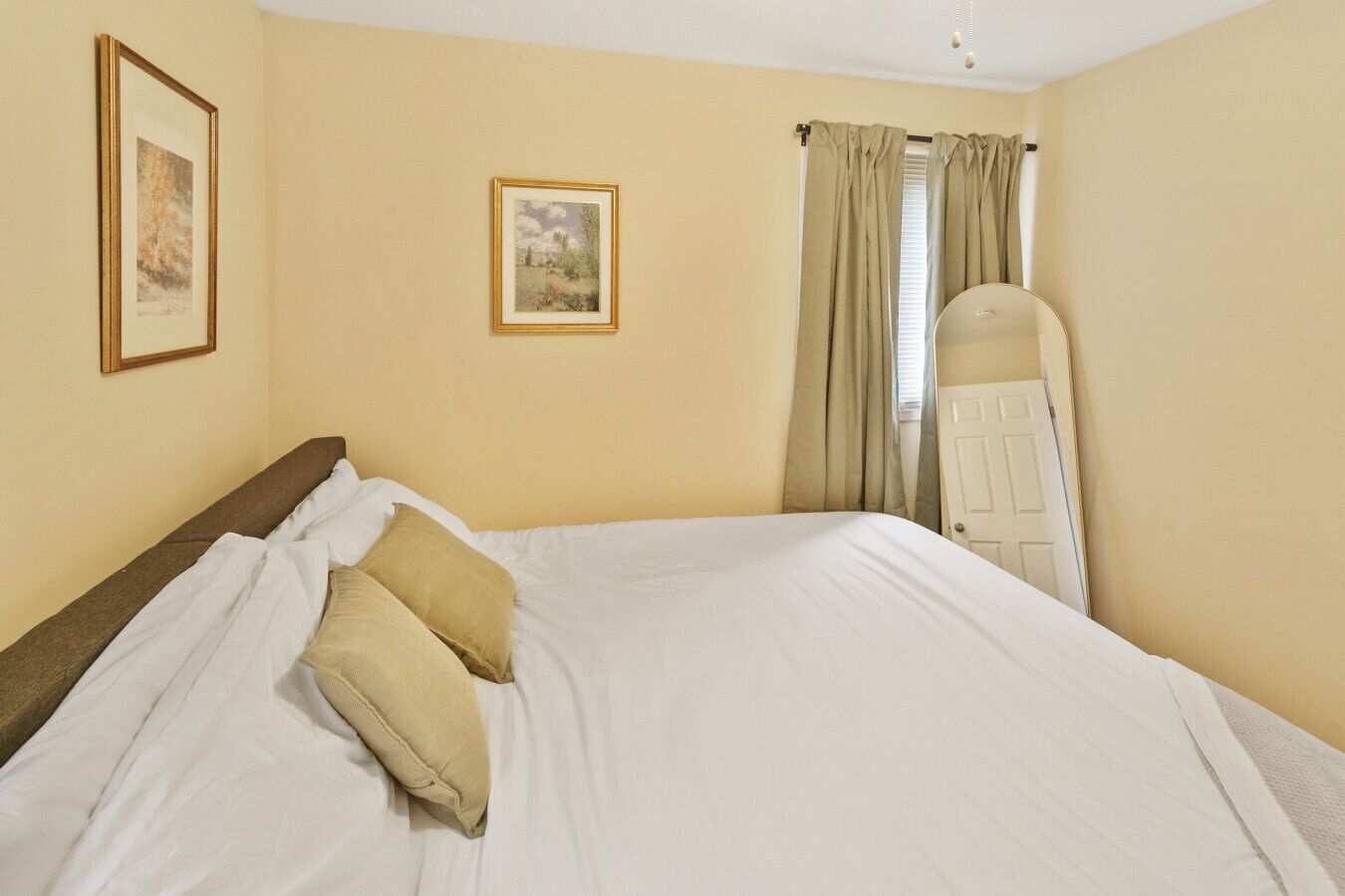 A hotel room with a large bed, two pillows, a headboard, a door, and two framed pictures on the wall.