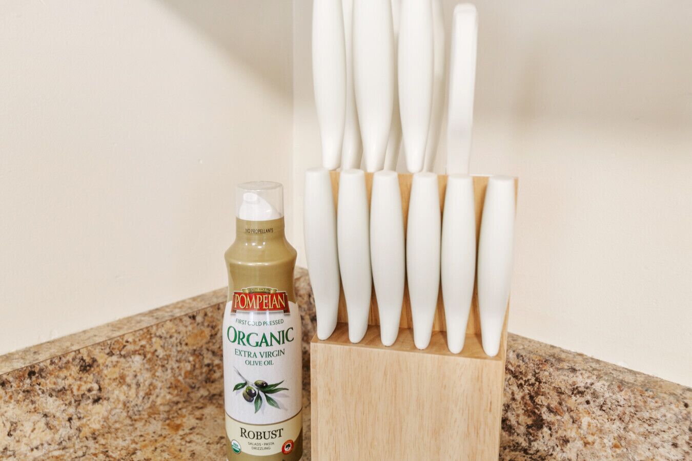 A bottle of organic extra virgin olive oil and a wooden knife block with several knives.