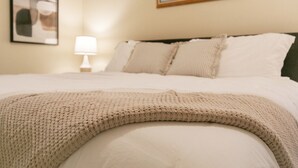 A neatly made bed with a knitted throw, a bedside lamp, and a framed abstract painting on the wall. - Sailor`s Escape with 3 bedrooms Near Naval Base! (Waukegan)