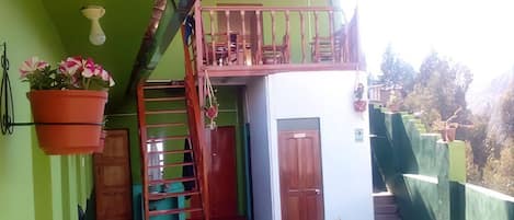 A balcony with a red railing, a small table with chairs, and a hanging flower pot.