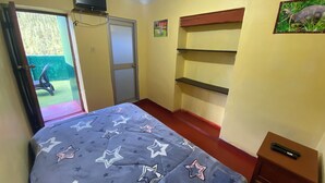 Een slaapkamer met een bed, een aan de muur bevestigde televisie, een deur naar een buitenruimte en een klein tafeltje met een afstandsbediening.