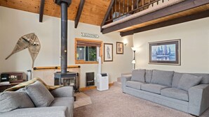A cozy living room with a fireplace, two grey sofas, a wooden ceiling, and a painting on the wall. - Hansel Getaway Chalet – Cozy A-Frame Near Leavenworth! (Peshastin)