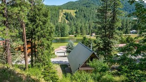 A cabin with a sloped roof, surrounded by dense forest and a lake. - Hansel Getaway Chalet – Cozy A-Frame Near Leavenworth! (Peshastin)