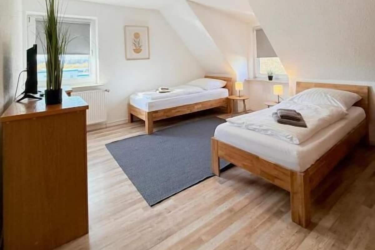 A small, well-lit room with two wooden beds, a desk, and a radiator.