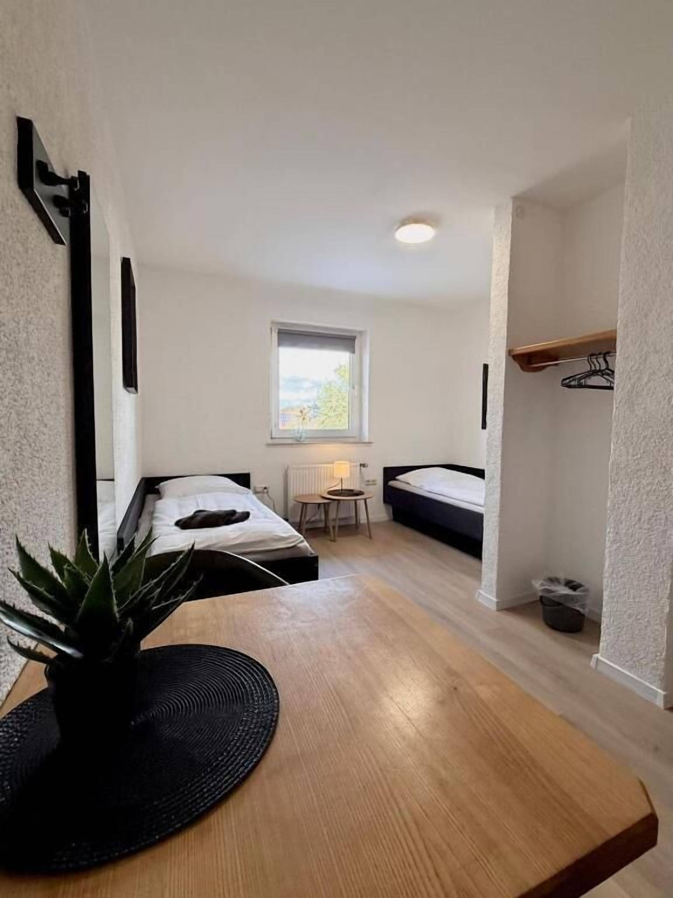 Habitación pequeña con dos camas, una mesita, una planta en maceta y ventana con vistas.