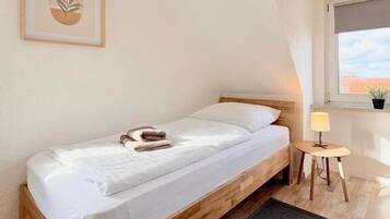 A single bed in a room with a sloped ceiling, a small table with a lamp, and a framed artwork on the wall.