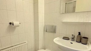 Ein kleines, sauberes Badezimmer mit weißen Fliesen, Toilette, Waschbecken und Spiegel.