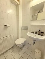 Un baño pequeño y limpio con azulejos blancos, inodoro, lavabo y espejo.