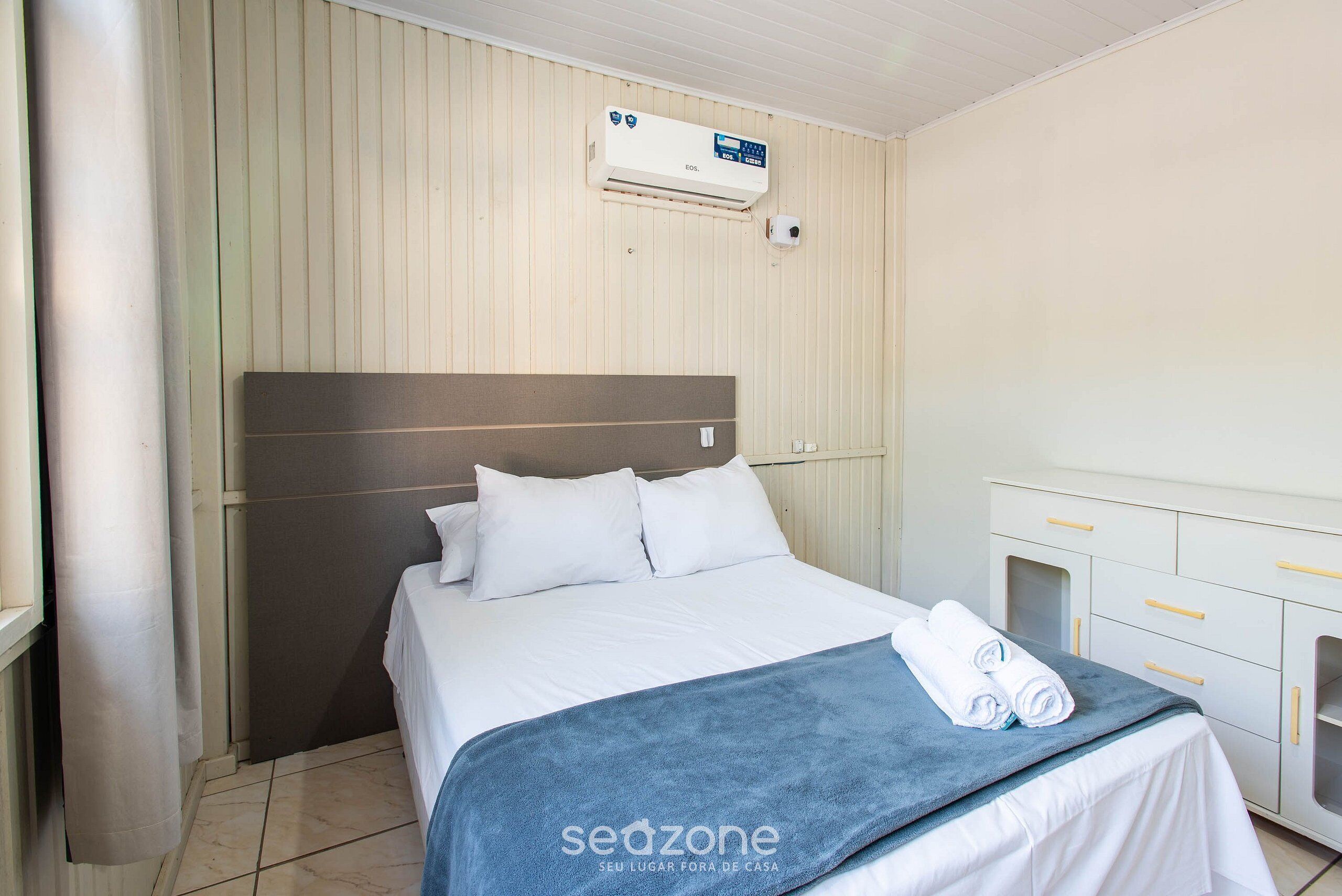 Quarto de hotel com cama, mesa de cabeceira, guarda-roupa e ar condicionado.