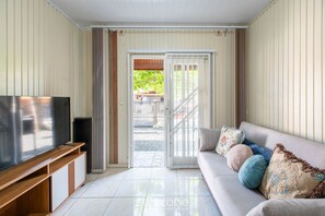 Ein Wohnzimmer mit Flachbildfernseher, einer Couch mit Zierkissen und einer Glastür, die zu einem Außenbereich führt.