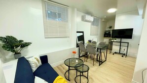 Een moderne woonkamer met een blauwe bank, een glazen salontafel en een eethoek met stoelen.