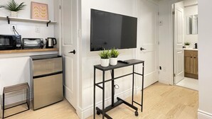 Een compacte keuken met een magnetron, broodrooster en koffiezetapparaat op het aanrecht, een koelkast, een aan de muur bevestigde tv en een kleine tafel met potplanten.