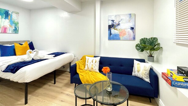 Een moderne hotelkamer met een bed, een slaapbank, een glazen bijzettafeltje en een potplant.