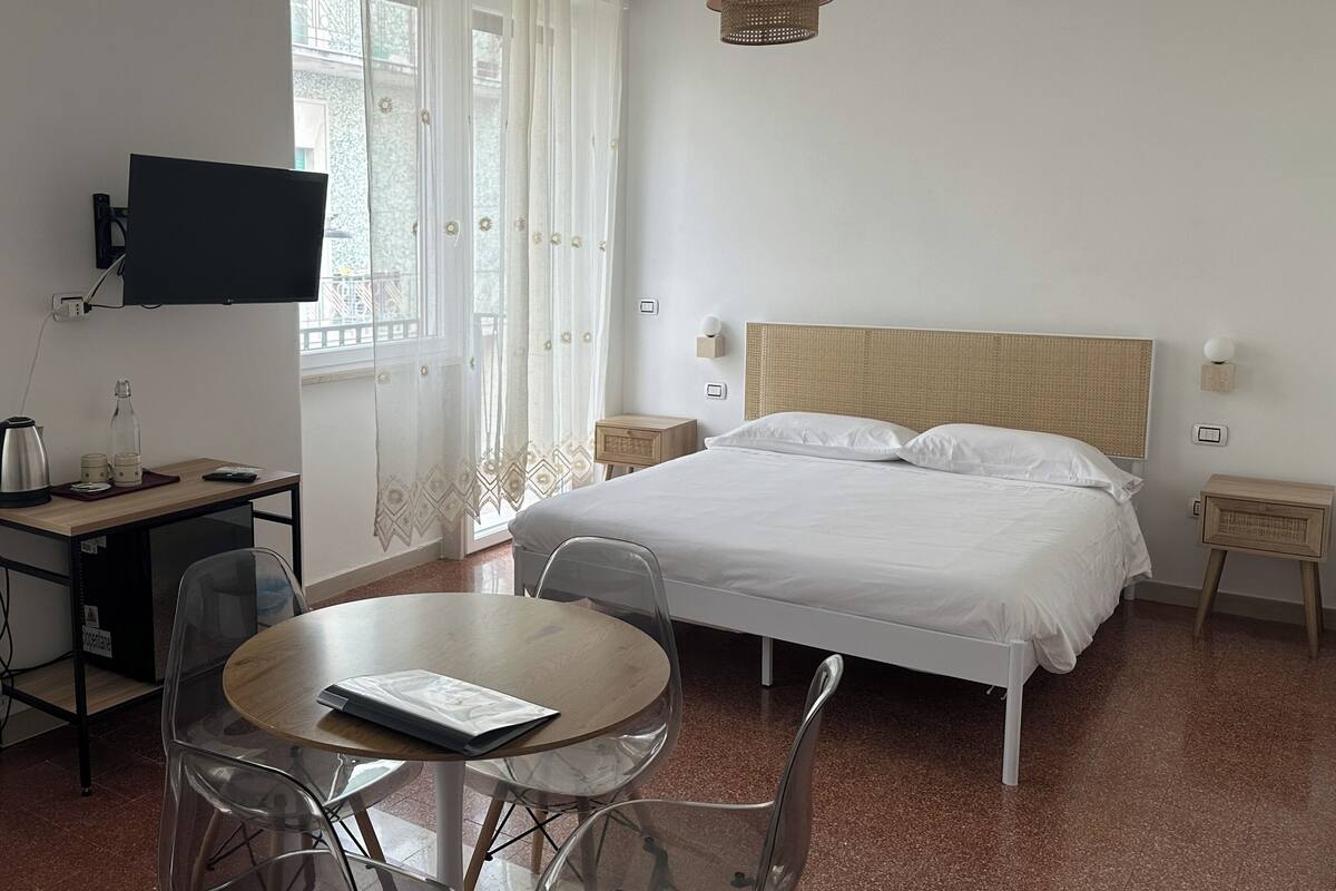 Ein Schlafzimmer mit einem Bett, einem Schreibtisch mit Fernseher, einem runden Tisch mit Stühlen und einer Hängelampe.