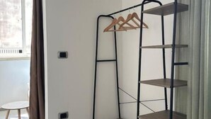 Une pièce avec une étagère métallique adossée au mur, une petite table et une fenêtre avec des rideaux.