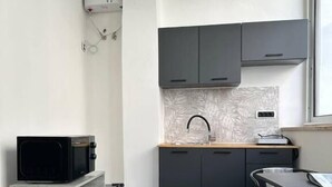 Une cuisine de taille réduite avec des meubles gris, un four à micro-ondes et une petite table à manger avec des chaises.