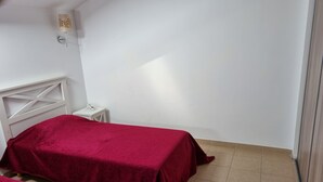 Ein Zimmer mit zwei Betten, die mit roten Decken bezogen sind, einem kleinen Nachttisch mit Lampe und einem weißen Kopfteil.