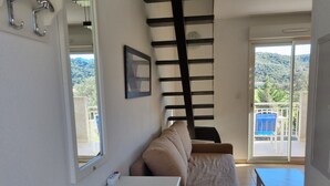 Ein kompakter Wohnraum mit Küchenzeile, einer Couch, einem Esstisch und einem Balkon mit Blick auf Grünflächen.
