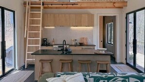 Una cocina moderna con una isla central, vigas de madera y una zona de dormir elevada.