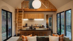 Una cocina moderna con armarios de madera, una isla central y un dormitorio entrepiso con escalera de madera.