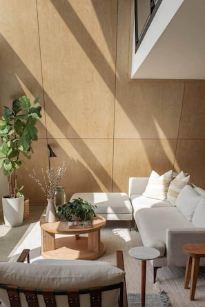 A modern living room with a sofa, coffee table, and chairs, a potted plant, and a vase with branches.