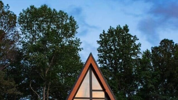 Un bâtiment triangulaire moderne doté de grandes fenêtres, d’une terrasse avec des chaises et entouré d’arbres.
