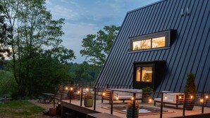 Une maison moderne avec un toit en pente, une terrasse dotée d’un espace salon extérieur et illuminée de guirlandes lumineuses.