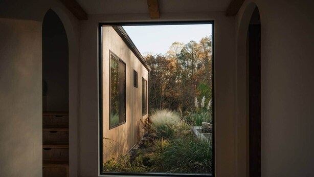 Un pasillo con un ventanal amplio, paredes de madera y vistas a un jardín.