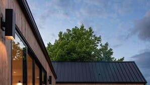 Una casa moderna con fachada de madera, amplios ventanales y un jacuzzi al frente.