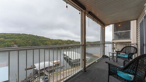 A balcony with a view of a lake and dock, furnished with wicker chairs and a table. - Cozy Lakefront 2BR Condo Near HH, Golf, Dining & The Strip (Lake Ozark)