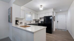 A modern kitchen with white cabinetry, a black refrigerator, and a microwave. - Cozy Lakefront 2BR Condo Near HH, Golf, Dining & The Strip (Lake Ozark)