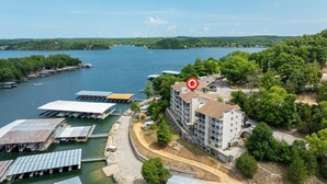 A waterfront hotel with multiple dock areas, a parking lot, and a building with a red arrow pointing to it. - Cozy Lakefront 2BR Condo Near HH, Golf, Dining & The Strip (Lake Ozark)