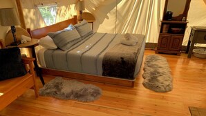 A cozy bedroom with a wooden bed, a small wooden nightstand, a fluffy rug, and a wooden bench.
