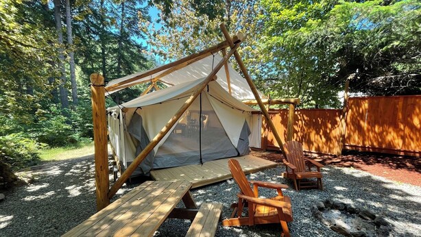 A tent with a wooden frame and a canvas cover, surrounded by gravel and wooden benches.