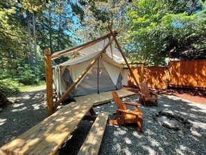 Una tenda con struttura in legno e copertura in tela, circondata da ghiaia e panche di legno.