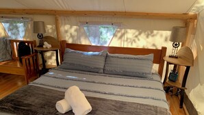 Een slaapkamer met een bed, twee nachtkastjes met lampen, een stoel en een raam met uitzicht op bomen.