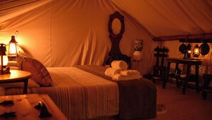 Een tentaccommodatie met een bed, een tafel met een lamp, een houten stoel en een kleine tafel met een lantaarn.