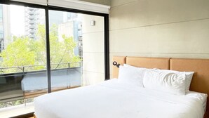 Ein modernes Schlafzimmer mit einem großen Bett, Blick auf die Stadt durch raumhohe Fenster und einem Balkon.
