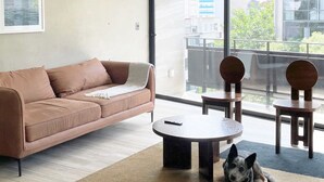 Ein modernes Wohnzimmer mit einer braunen Couch, einem runden Couchtisch und zwei Holzstühlen. Ein Hund liegt auf dem Boden.