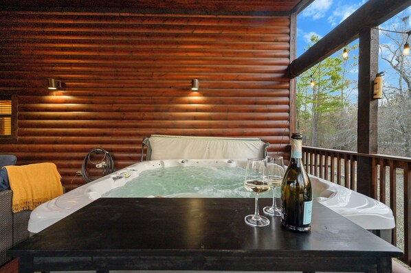 En træhytte med jacuzzi, to vinglas og en flaske på et bord.