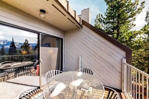 A modern outdoor patio with a round table and chairs, a glass door leading to a deck, and a view of trees and mountains. - Eagle's Nest - Condo in Huntington Lake (Big Creek)