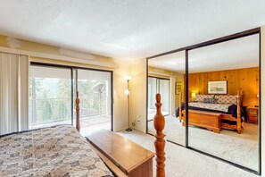 A bedroom with a large bed, a wooden bench, a floor lamp, and a view of a balcony. - Eagle's Nest - Condo in Huntington Lake (Big Creek)