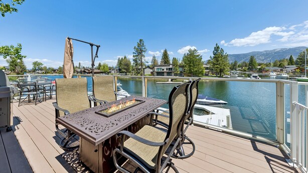Eine Terrasse mit Gartenmöbeln, einer Feuerstelle und Blick auf einen See mit Booten und Bergen im Hintergrund.