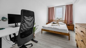Un dormitorio moderno con una cama de madera, un escritorio con una computadora y una silla.