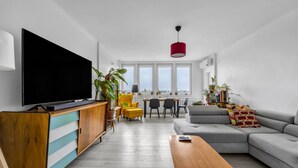 Una sala de estar moderna con un televisor de pantalla plana grande, una mesa de centro de madera, un sofá gris y una zona de comedor con mesa y sillas.
